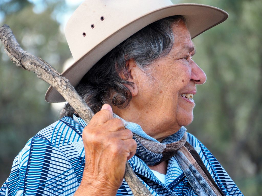 Aboriginal woman wearing a hat and holding  a stick